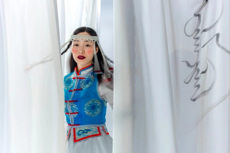 a girl dressed in traditional chinese garb looking out from behind the curtain