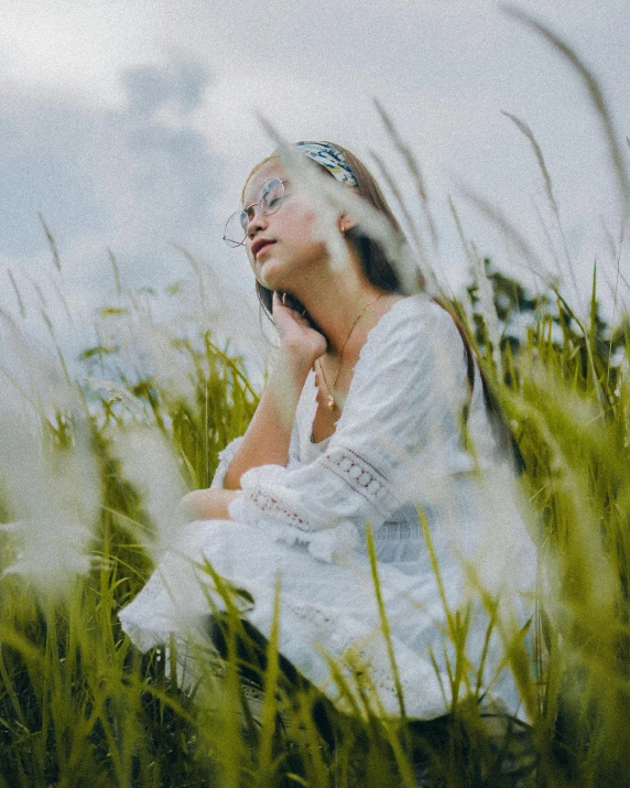 a woman sitting in tall grass with her eyes closed