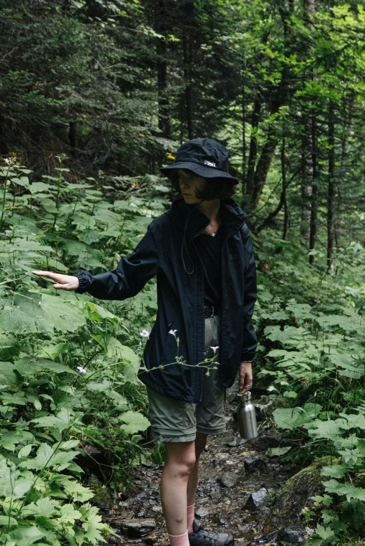 a person with a hat, rain jacket and hiking boots is walking through the woods