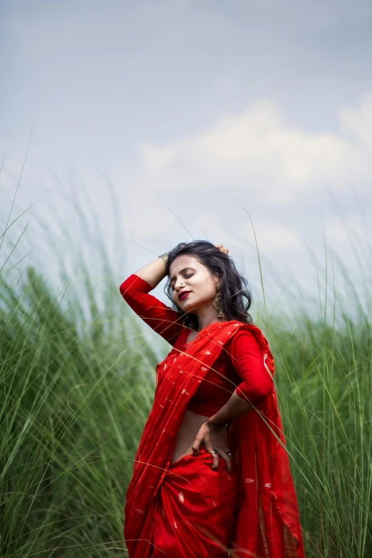 a woman with red clothing and long hair is standing by tall grass