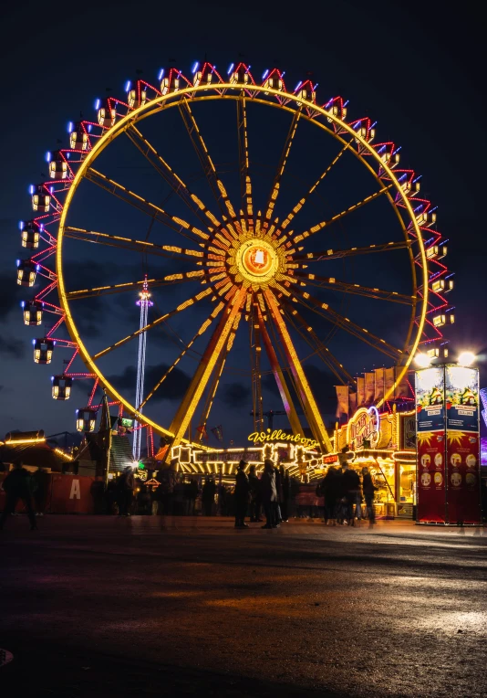 an outdoor lighted ferris wheel with buildings in the background