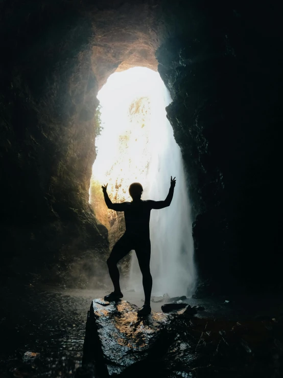 man standing in front of waterfall with arms in the air