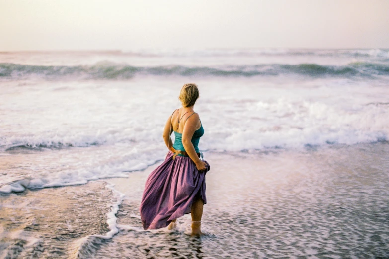 a woman stands on the shore looking at the ocean