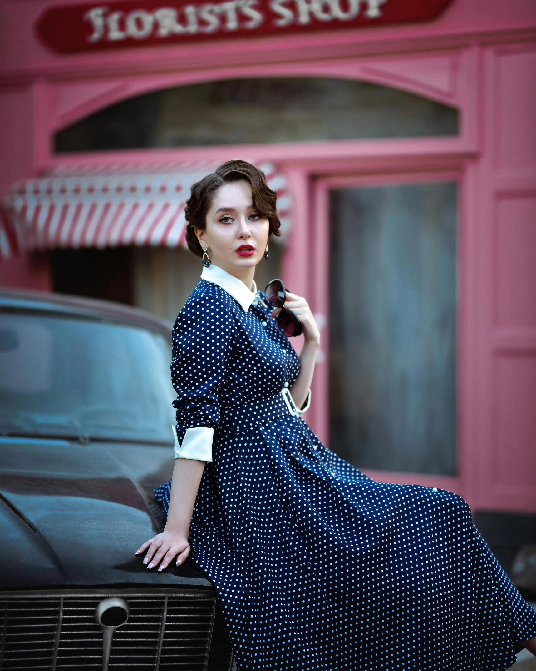 a woman in a dress leaning on the hood of a car