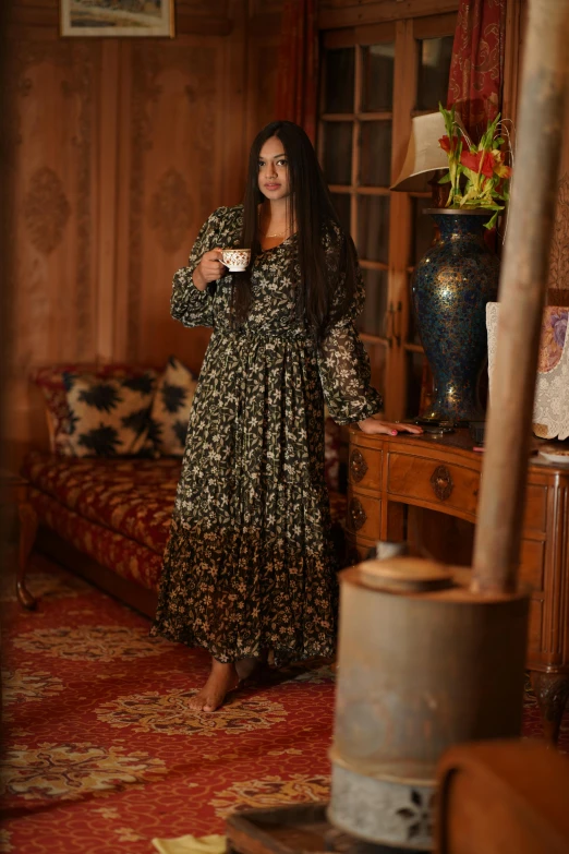 a beautiful woman standing next to a table holding a cup