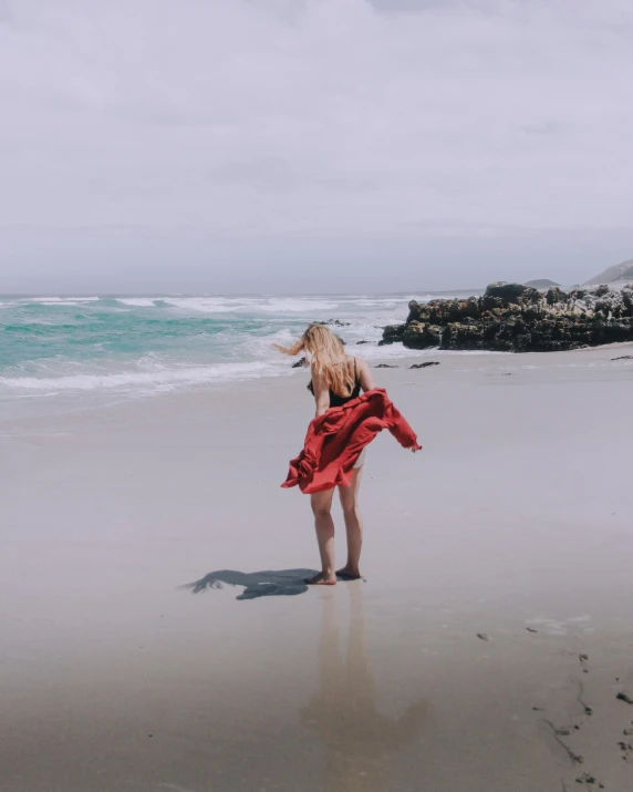 a woman in a red dress walking on the beach with her dog