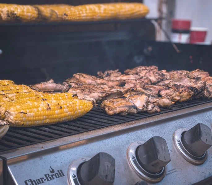 the grill is filled with grilled corn and chicken