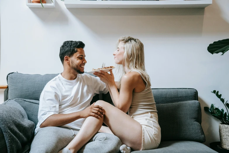 a couple having pizza while sitting on a couch