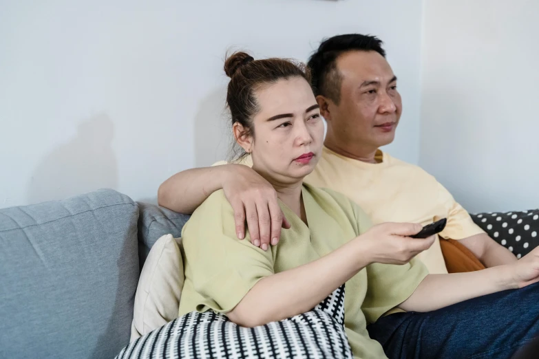 a young man and woman sitting on a couch looking at a remote