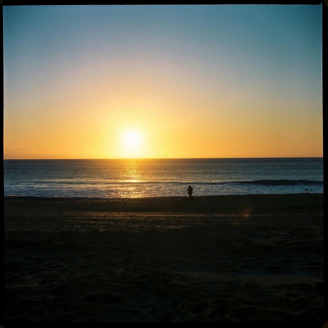 a man is walking along the beach at sunset