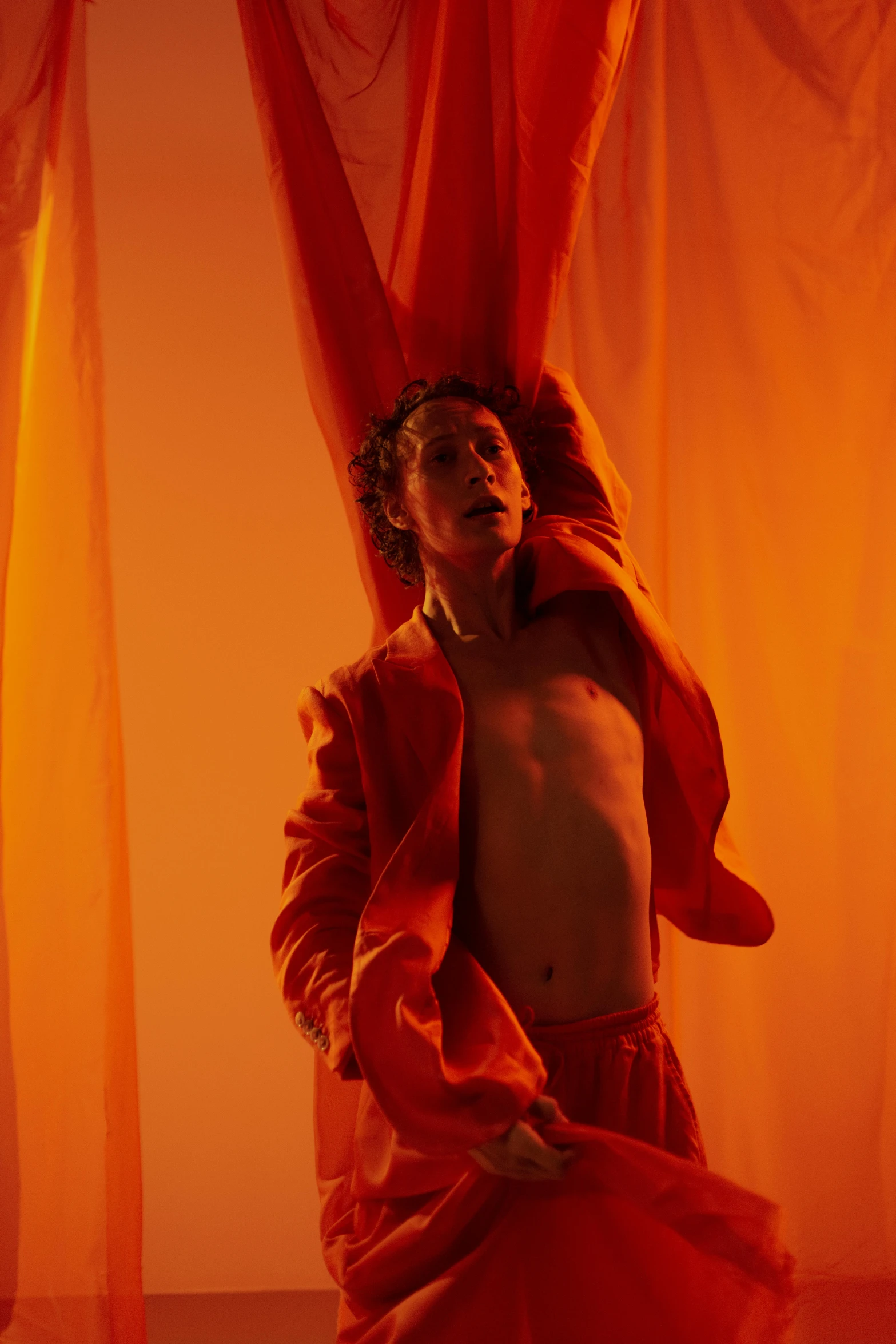 a man in a red tutu poses underneath curtains