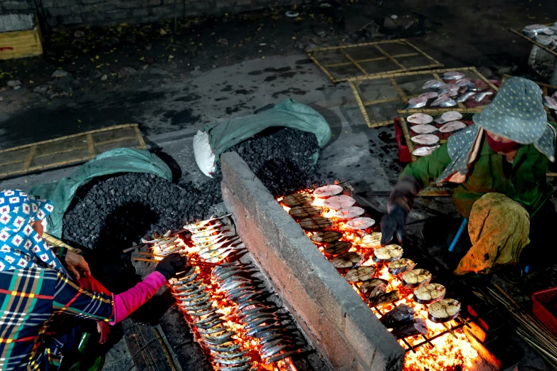 people are cooking food on small grills in the street