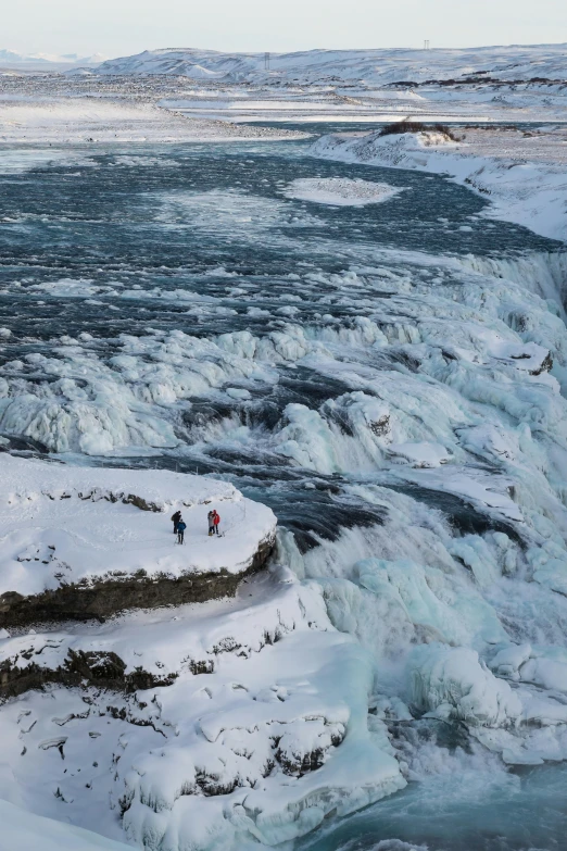 two people walking in the snow in front of a waterfall