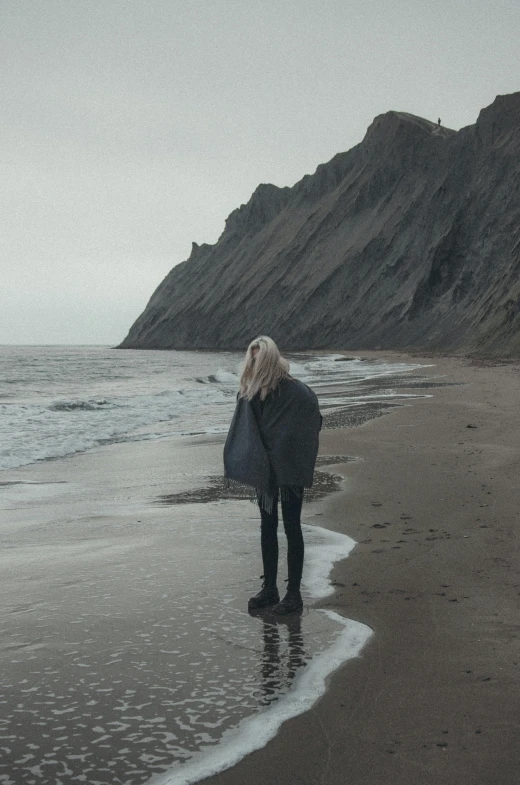 a person in black jacket standing on beach with water