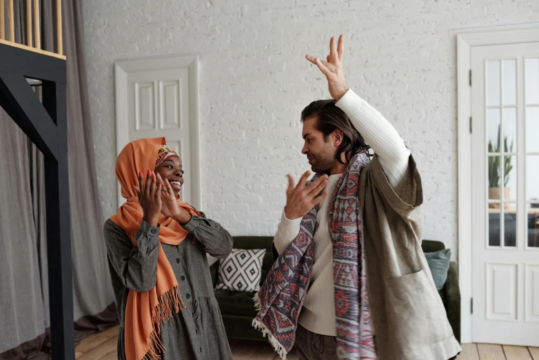 a woman and man standing in the middle of a room with their arms spread in the air