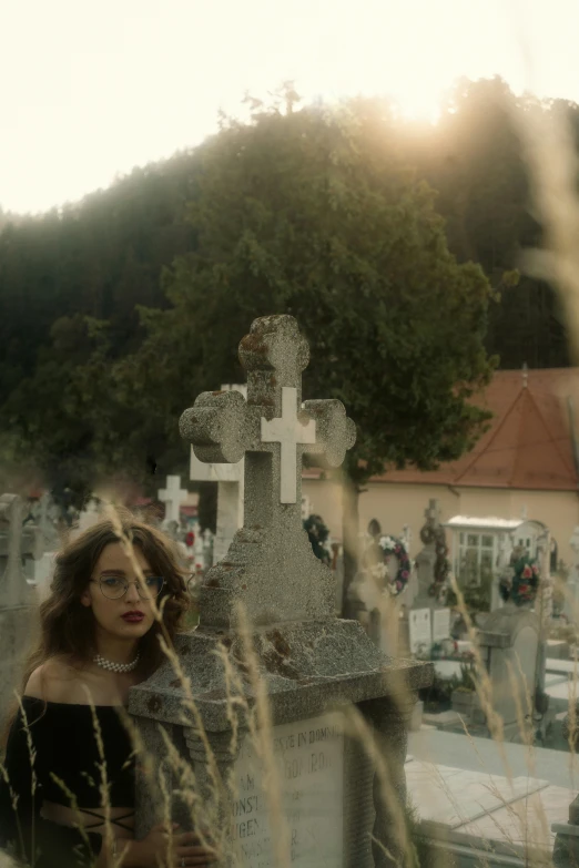 a woman with glasses next to a grave with a cross