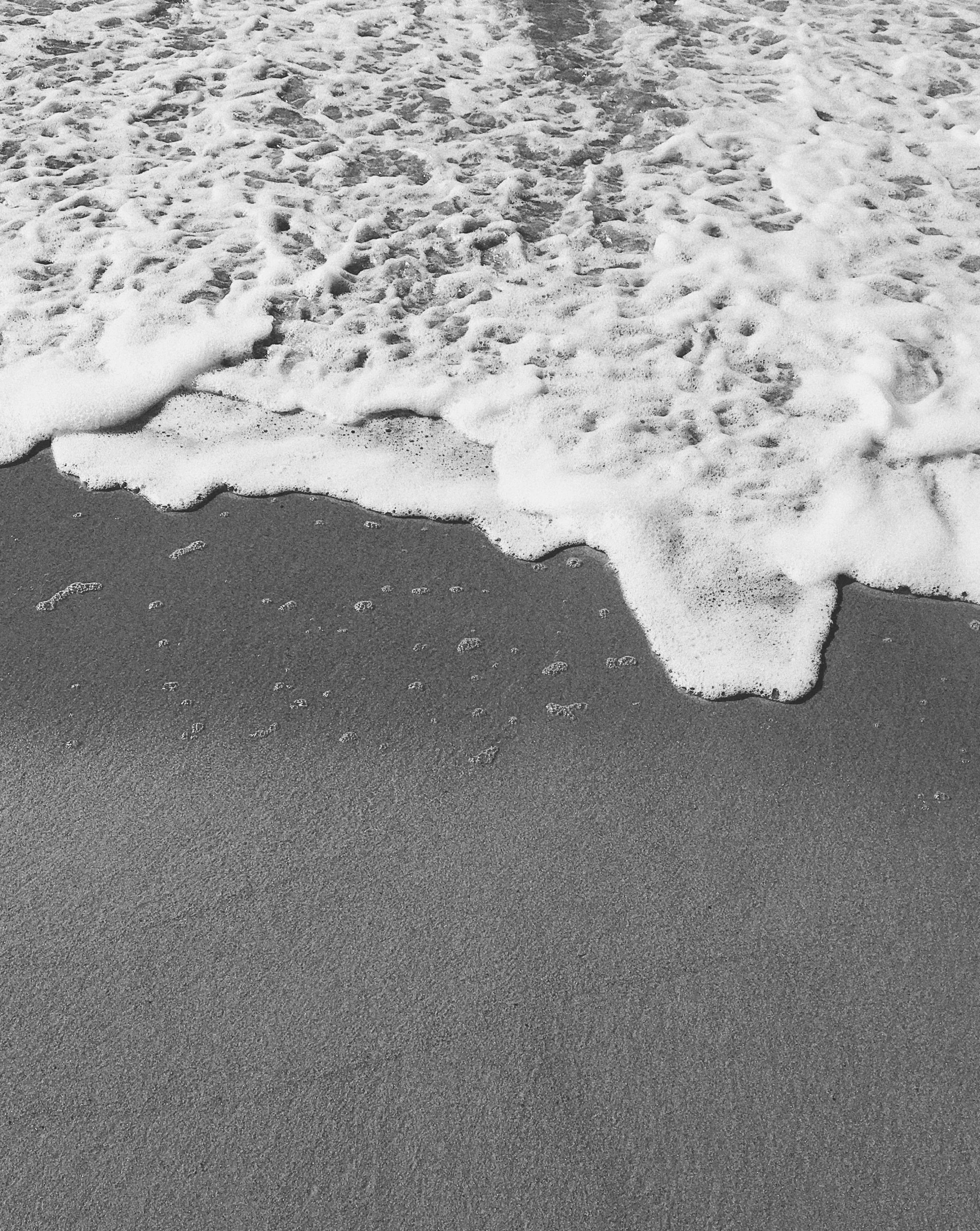 white foamy wave coming towards the shore of an ocean beach