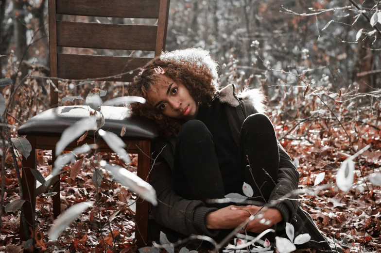 a woman sitting on a wooden chair in the middle of a forest