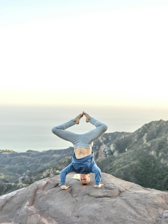 a woman doing a yoga position on top of a mountain