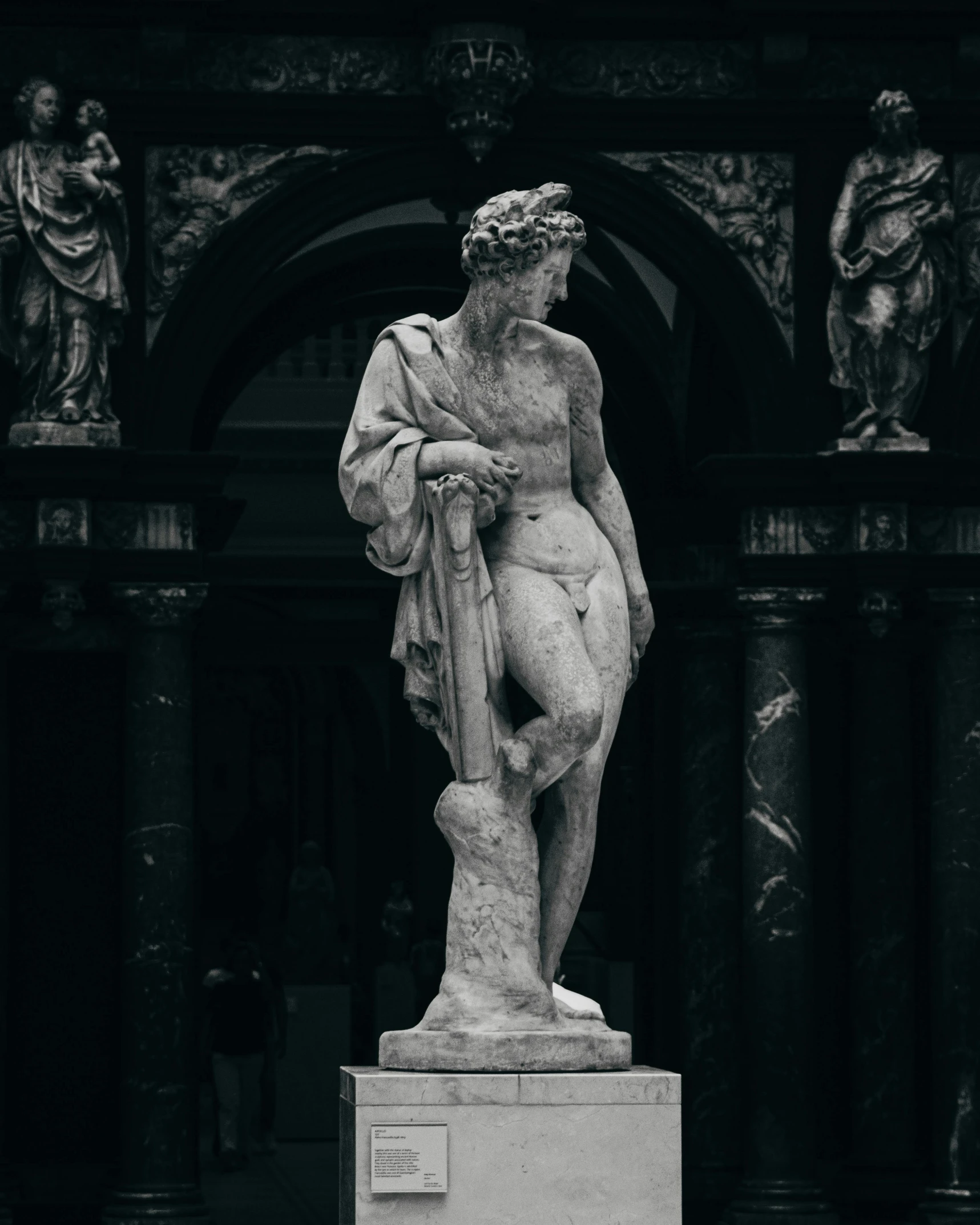 statue stands in front of a building while people walk near by