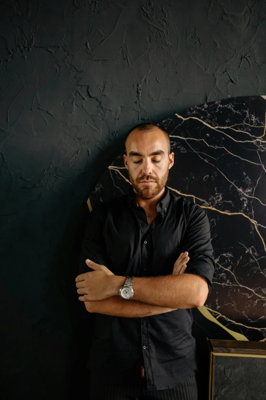 a man in black shirt leaning against black wall