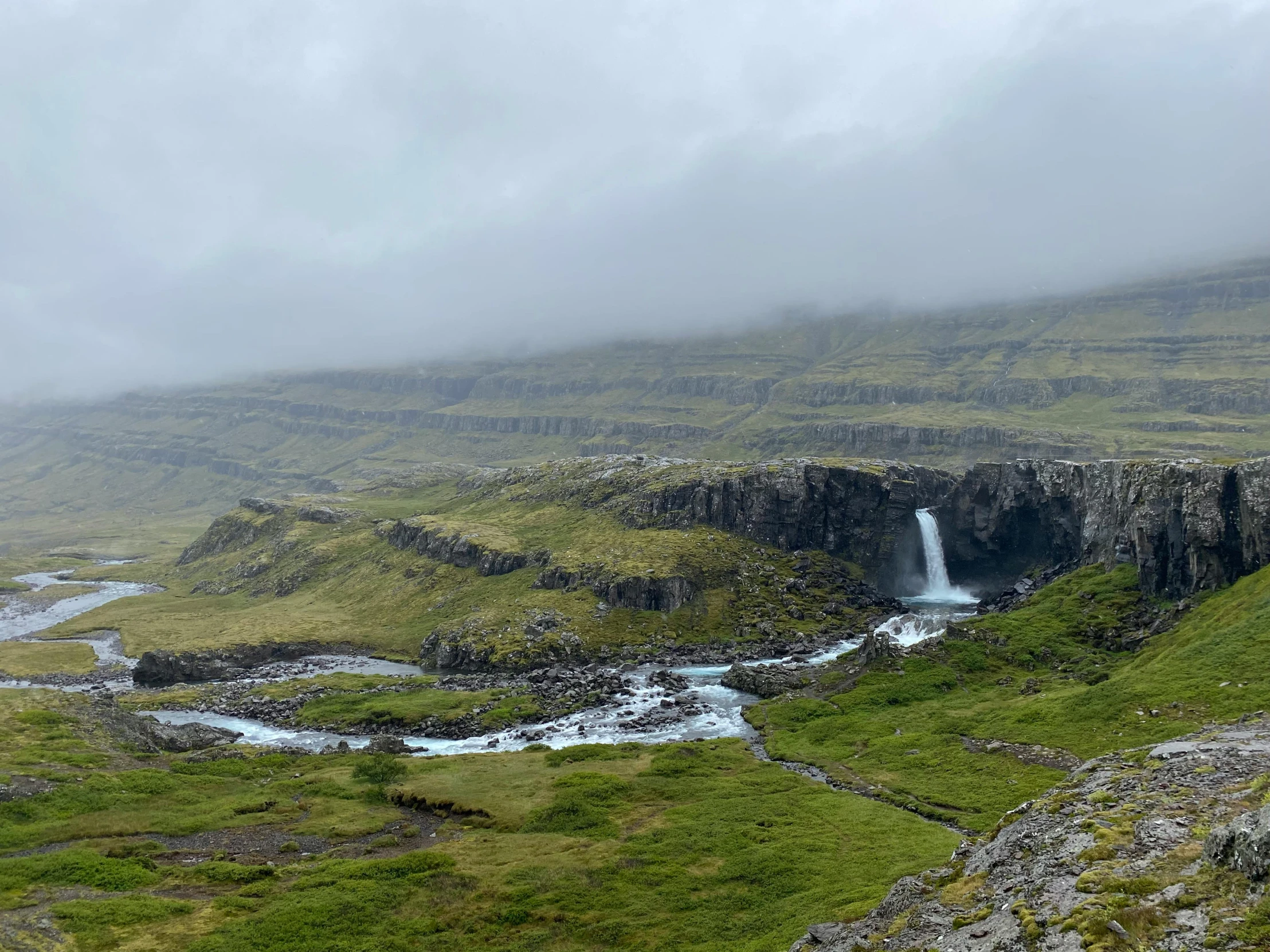 a river flowing into a small pool next to lush green hillside