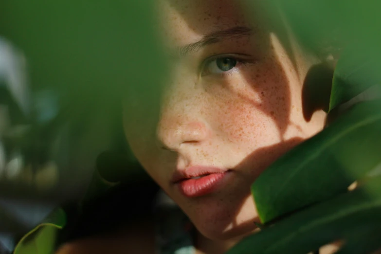 a close up of a child's face and green leaves