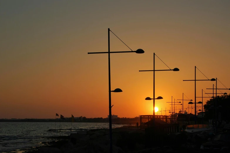 a sunrise near the ocean with tall poles and birds