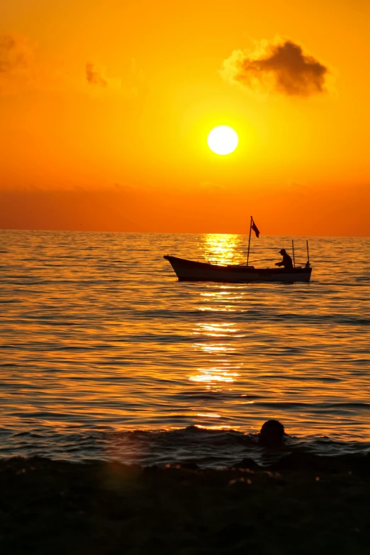 the sun setting on a calm ocean with a small boat