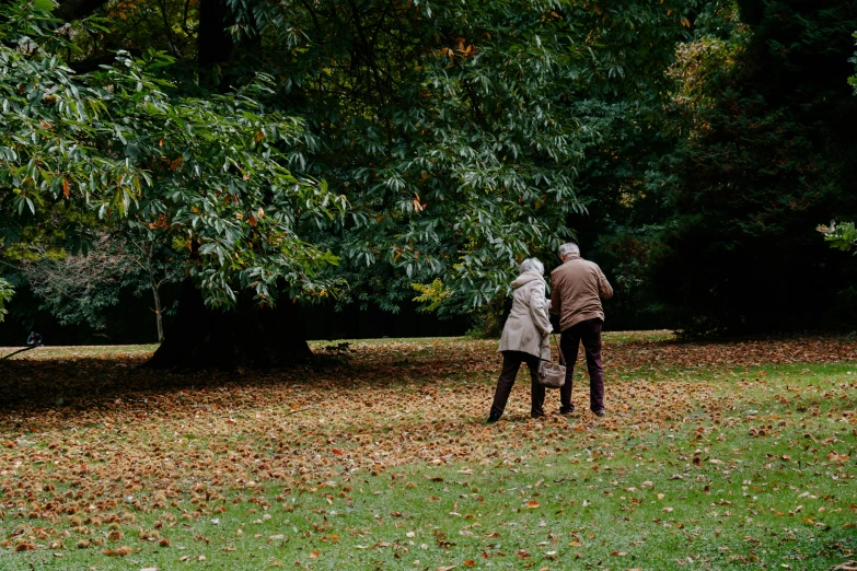 a man and woman walking through a park on top of leaves