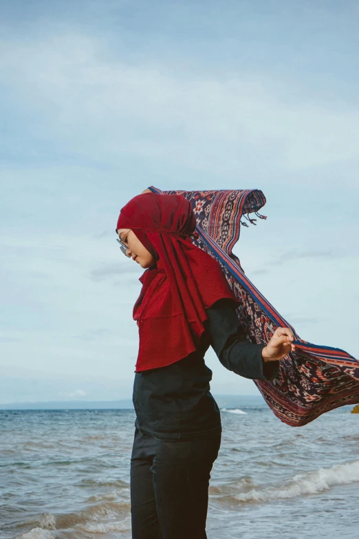 a woman in red hijab standing on beach with waves