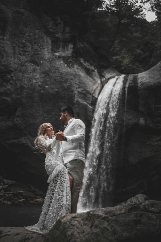 a man and woman are standing near a waterfall