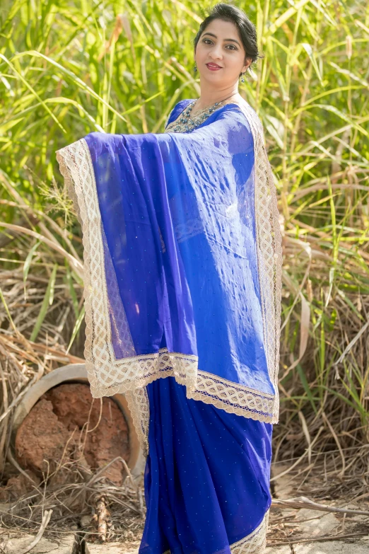 a woman with a large blue sari stands in front of a tree