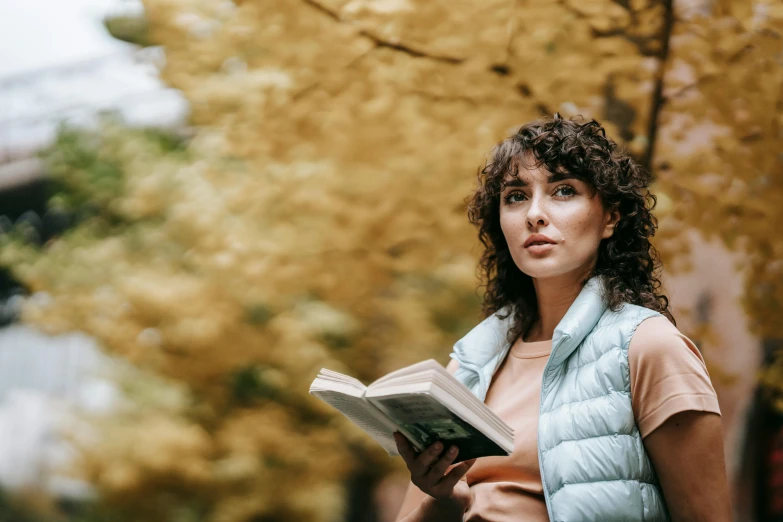 woman with long hair and blue vest holding a book