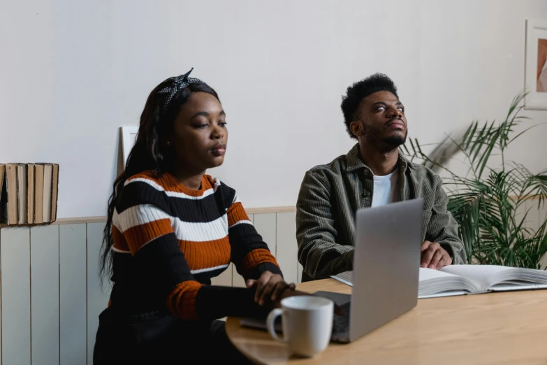 two people sitting at a table and working on laptops