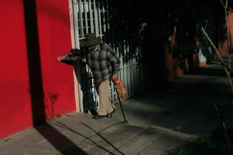 the man in plaid shirt and hat walks on sidewalk