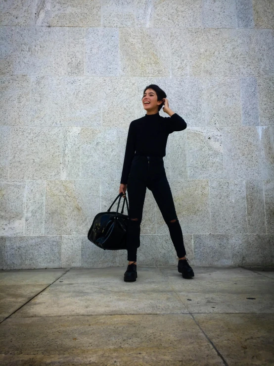 a woman standing near a building holding a purse while talking on the phone