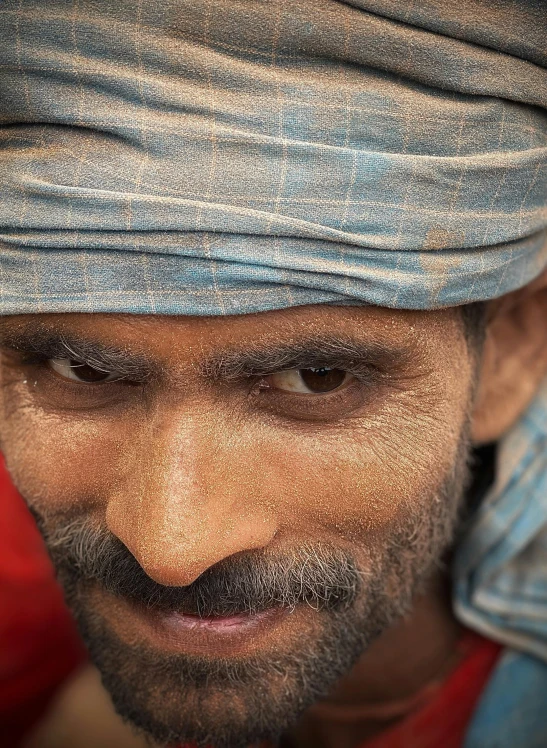 a man with grey hair wearing a red shirt and blue turban