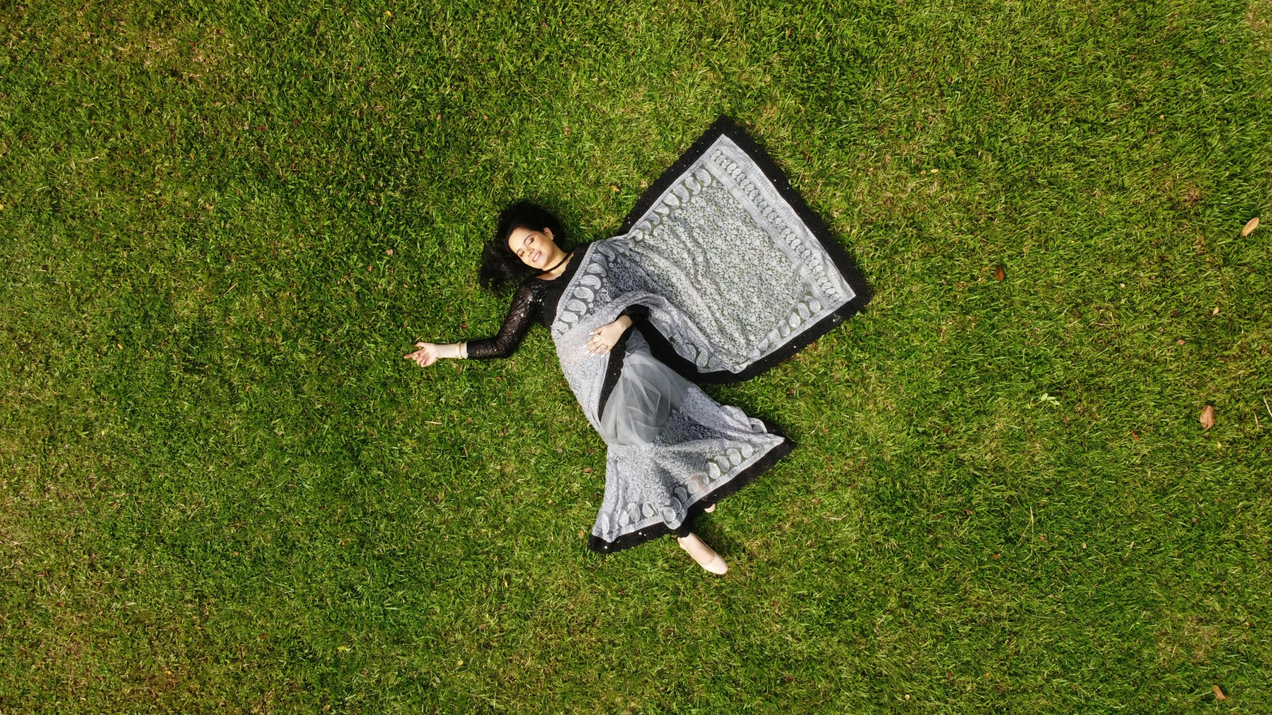 a woman laying on the grass with a large umbrella