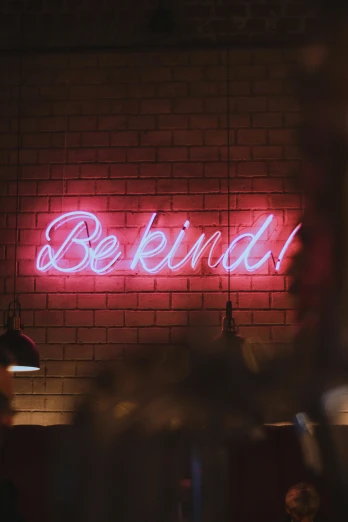 a neon sign that reads be kind on a brick wall