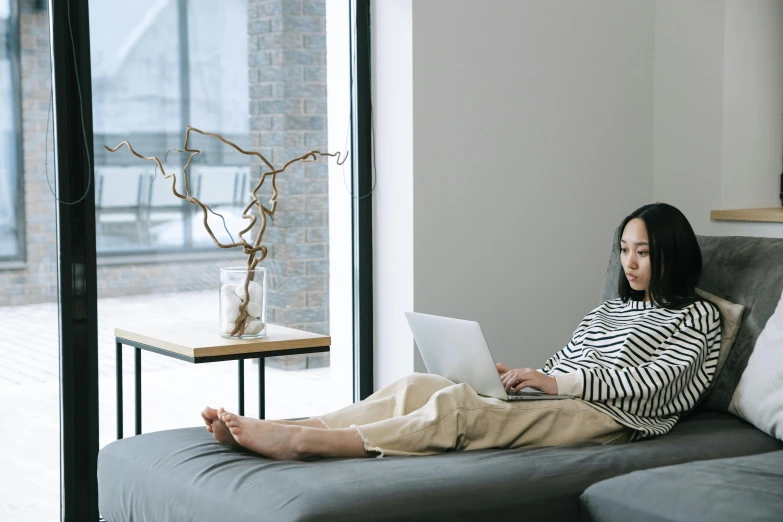 a woman with dark hair and white shirt is sitting on the couch using her laptop