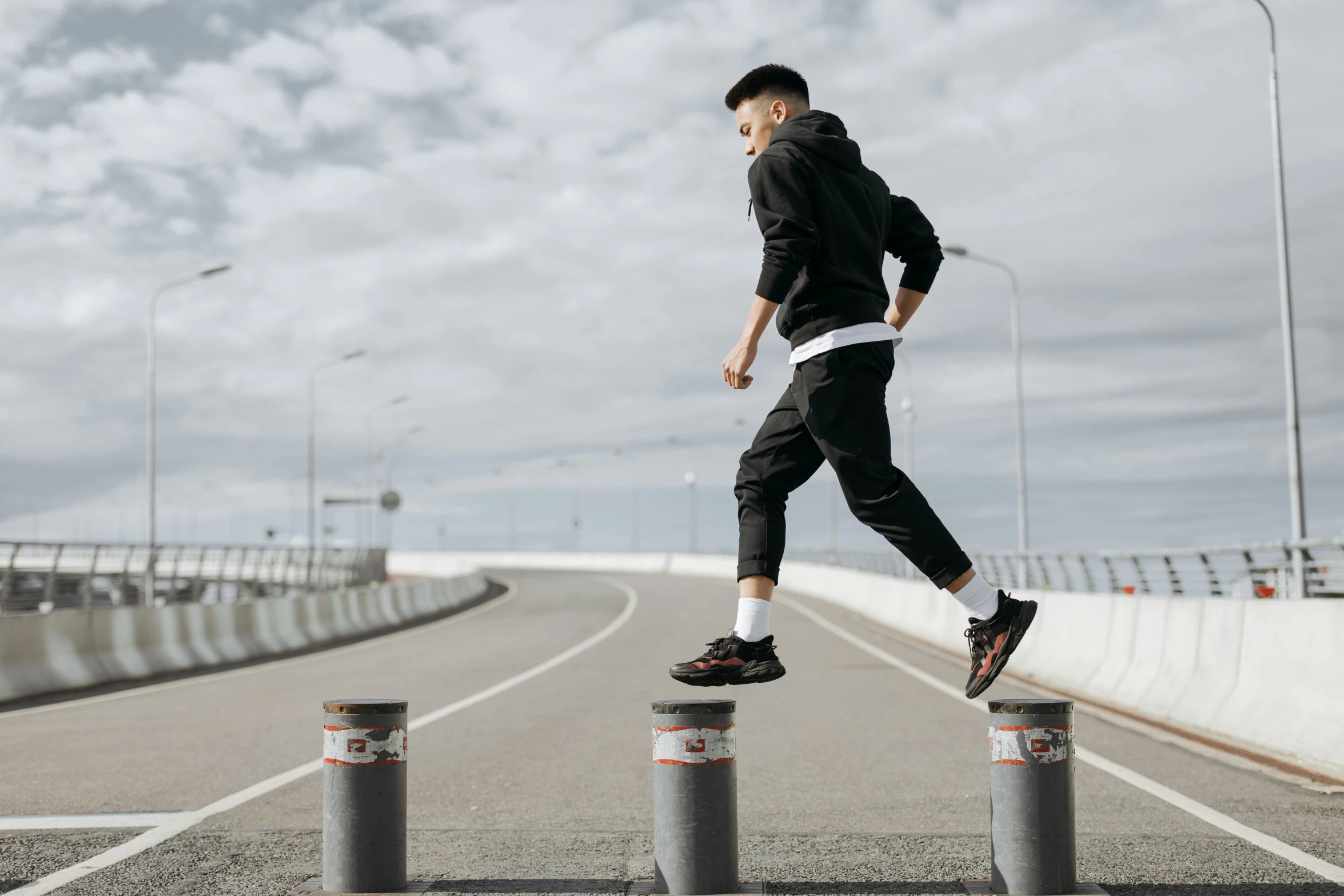 the man in a black hoodie is jumping over three metal posts