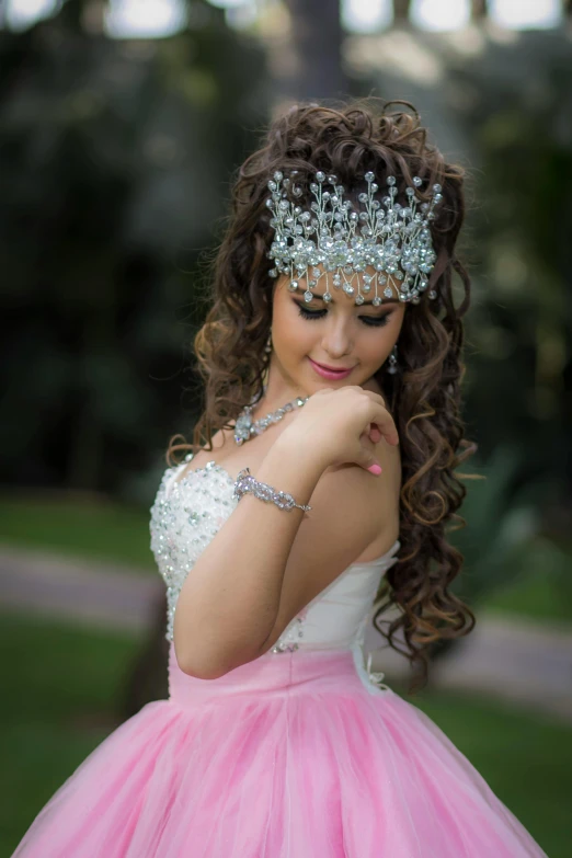 a young woman wearing a tiara and dress standing in a park