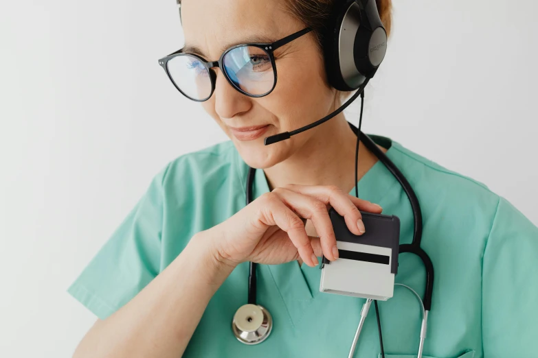 woman doctor wearing headset, green scrub and with headphones holding a cd