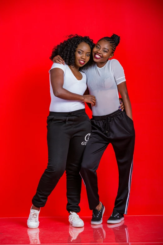 two black women, one in white and the other in black, stand next to each other against a red background