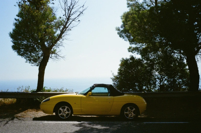 a yellow sports car is parked on the side of a road near trees