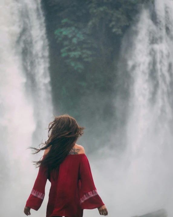 a woman wearing red and standing in front of waterfall