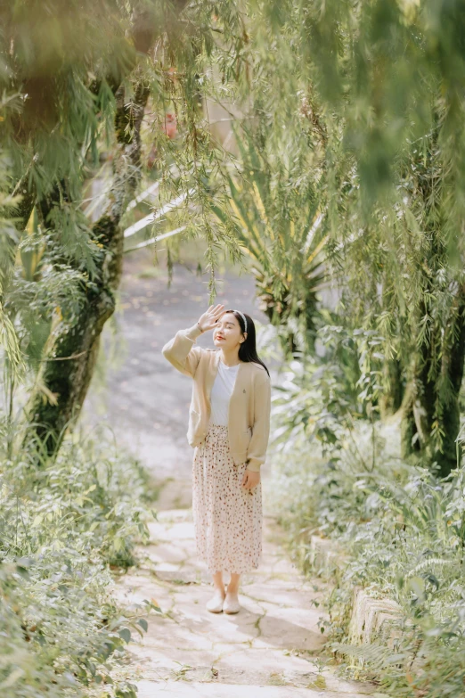 a girl standing in front of trees with her arms on her head and looking up