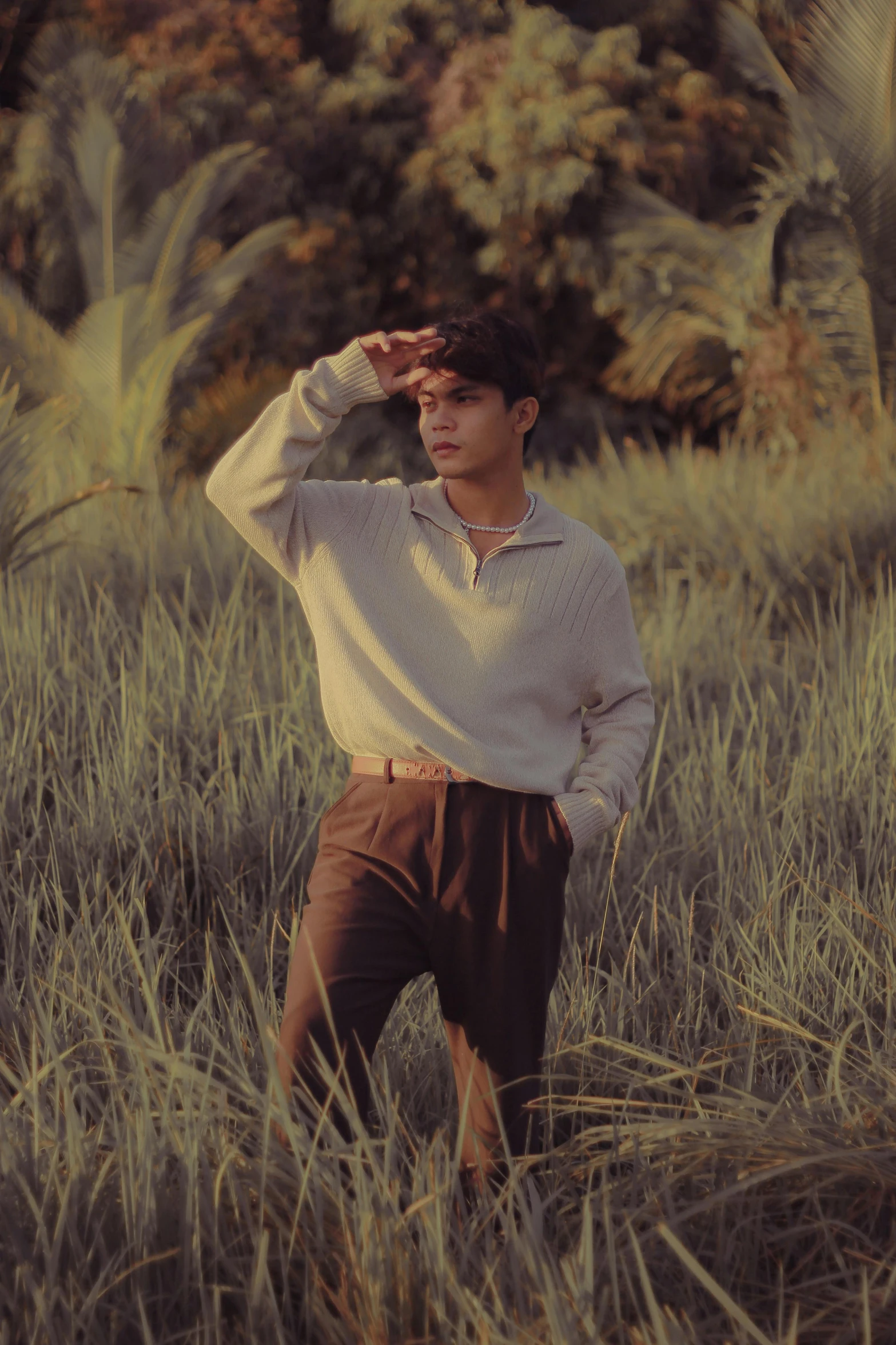 the man in brown shorts is wearing a sweater and standing among tall grass