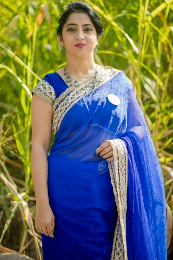 a woman wearing a saree and jewelry in front of grass